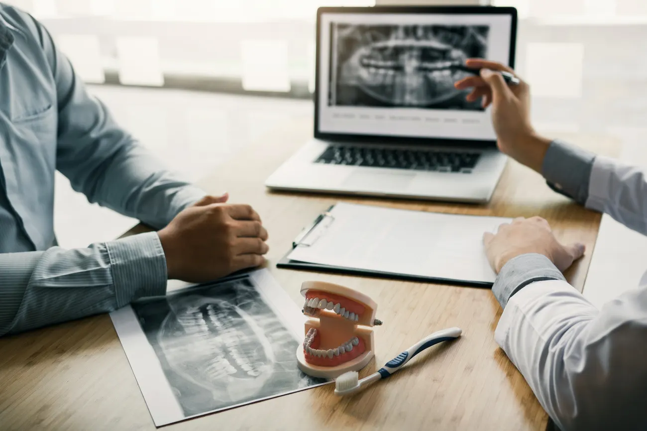 Dentists are discussing dental problems at report x-ray image on laptop screen to patients.